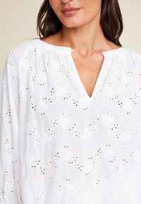 Hvit bluse laget av lett stoff, med broderi og V-hals. Litt puffede ermer og avslappet passform.