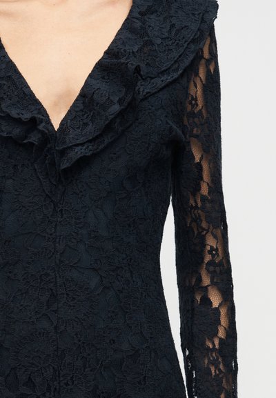 Melna mežģīņu kleita ar ziedu rakstu, dziļu V veida rievotu apkakli un caurspīdīgām garām piedurknēm.