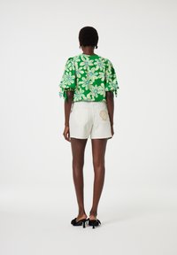 Groene top met bloemenpatroon en ruches aan de mouwen, gecombineerd met witte shorts met een golvende zoom en een schelpenborduursel op de zak.