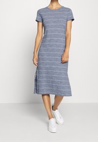 Robe t-shirt à rayures bleues en tissu doux, avec des manches courtes, un col rond et une fente sur le côté, portée avec des baskets blanches.