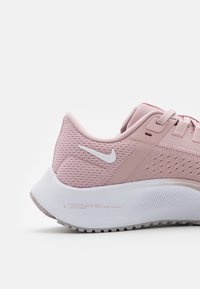 Zapatilla de running en rosa claro con una parte superior de malla texturizada, acentos blancos y una suela blanca acolchada que presenta una suela con patrón.