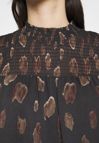 Robe en tissu noir avec des taches abstraites marron et beige et un col montant froncé, vue des épaules jusqu'à la partie supérieure de la poitrine.