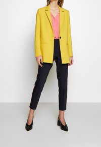 Žlutý blejzr s klopami, spárovaný s růžovou blůzou a námořnickými kalhotami s bočními pruhy. Doplněno černými lodičkami na podpatku.