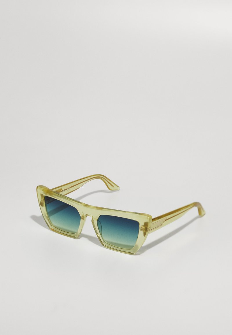 Gelbtönte Sonnenbrille mit rechteckiger Form und blauen Verlaufslinsen. Verfügt über dicke transparente Rahmen und gerade Bügel.