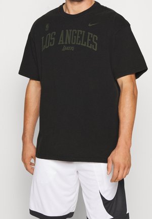 Man draagt een zwart Los Angeles Lakers T-shirt en witte basketbalshorts met een zwart Nike-swooshlogo op het linkerbeen.