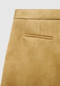 Yellow suede fabric close-up featuring a smooth texture and a single back pocket with a clean edge. Subtle stitching visible around the waist.