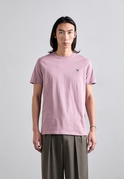 Tricou roz deschis din bumbac moale, cu guler rotund și un mic motiv brodat pe partea stângă a pieptului, asortat cu pantaloni plisati.