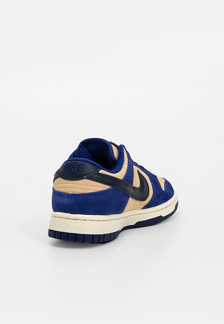 Las zapatillas Nike Dunk presentan una parte superior de ante azul con acentos en marrón, un swoosh negro y una suela de goma texturizada. Diseño clásico de corte bajo.