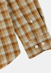 Tissu de chemise à carreaux marron et beige, doté d'un poignet à boutons avec des boutons blancs et d'un motif texturé sur l'ensemble du matériau.