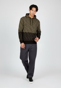 Olijfgroen hoodie met een zwarte ondersectie. Kenmerkt zich door een herhalend patroon, geribbelde manchetten en een kangoeroezak. Gecombineerd met grijze broek.