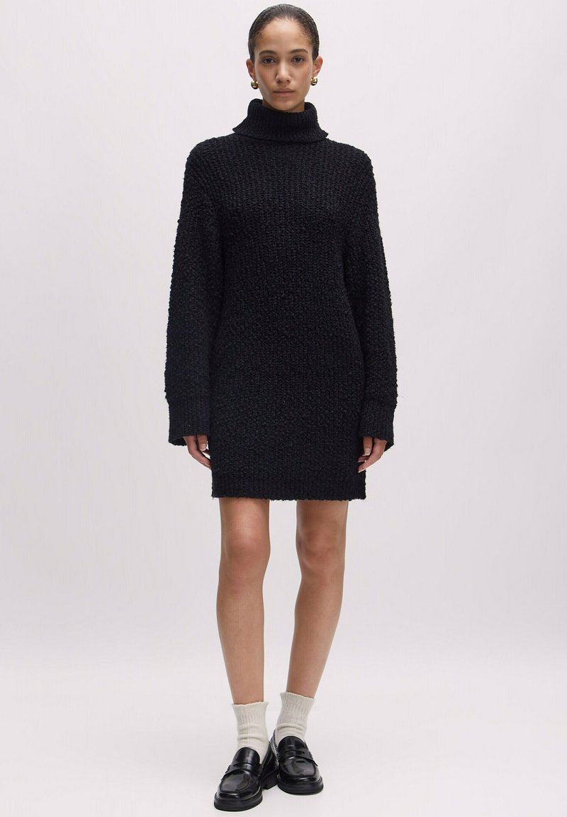 Schwarzes gestricktes Kleid mit hohem Rollkragen, langen Ärmeln und lockerer Passform, das ein strukturiertes Muster und ein geripptes Saumdesign aufweist.