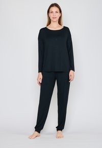 Černý dlouhý rukáv s kulatým výstřihem, kombinovaný s odpovídajícími černými zúženými kalhotami. Měkká tkanina; ležérní, uvolněný silueta.