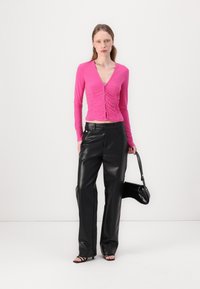 Pink long-sleeve top with a V-neck and button front, paired with high-waisted black faux leather pants and a small black handbag.