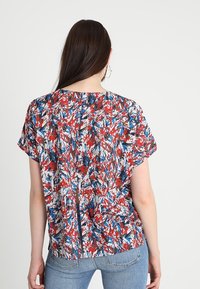Blusa multicolore con un vivace motivo astratto in rosso, blu e bianco; vestibilità rilassata con maniche corte e dettaglio di spacco sul retro.