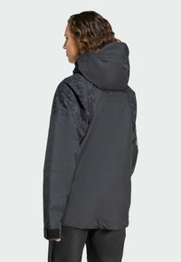 Svart vattentät jacka med texturerade svarta axeldetaljer, justerbar huva och kardborrefästen vid ärmslut, designad för utomhusbruk.