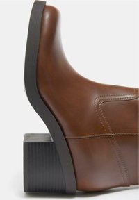 Botină maro din piele, cu toc bloc negru suprapus și detalii vizibile de cusături pe părțile laterale și spate.