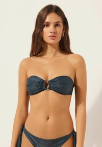 Dunkelblauer Bandeau-Bikini-Oberteil mit gerafftem Stoff, zentralem Strassakzent und glatter Textur. Kombiniert mit einer Hose mit seitlicher Schnürung.