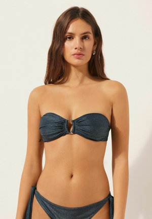 Haut de bikini bandeau bleu foncé avec tissu froncé, accent central en strass, et texture lisse. Associé à un bas à nouer sur le côté.