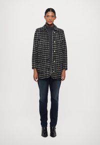 Chaqueta a cuadros en blanco y negro con cuello, dos bolsillos frontales y botones, combinada con jeans oscuros y botas de tobillo negras.