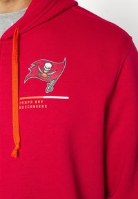 Rød hættetrøje med Tampa Bay Buccaneers logo, orange snor og hvid horisontal stribe med teksten "TAMPA BAY BUCCANEERS".