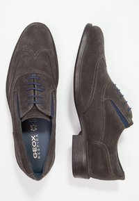 Chaussures habillées en daim gris au design élégant, avec des lacets bleus, des coutures détaillées, un bout arrondi et un talon bas et arrondi. Marque Geox visible.
