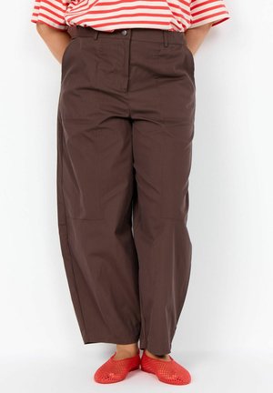 Person wearing brown wide-leg pants, red mesh slip-on shoes, and a red and white striped shirt with hands behind their back.