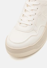 Sneaker bianca in pelle con suola in gomma testurizzata, forma arrotondata e design con lacci; presenta cuciture sottili e un branding minimale.