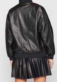 Svart läderbomberjacka med en slät textur, ribbade ärmslut och nederkant. Kombinerad med en plisserad svart kjol med glänsande tyg.