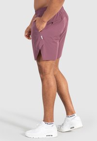 Lätta, mauve shorts med elastiskt midjeband, sidofickor och en delad design för rörlighet. Matchas med vita sportskor.