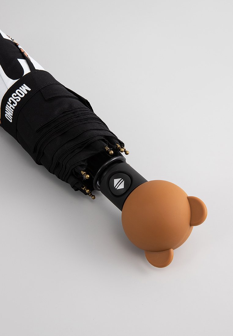 Ombrello compatto nero con manico a forma di orso bruno, realizzato in materiale silicone flessibile e con punte in metallo color oro sulle stecche, caratterizzato da dettagli con logo.