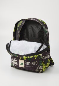 Mochila con un diseño floral oscuro en verde y blanco, con un compartimento principal con cremallera y un parche de logo en la parte frontal.