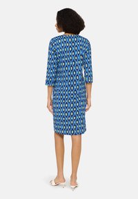 Blaues Kleid mit geometrischem Muster in Grün und Schwarz. Mit 3/4-Ärmeln, knieumspielender Länge und rundem Ausschnitt. Glatte Textur.