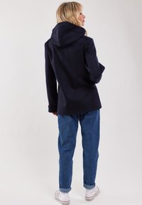 Mörkblå huvjacka med en mjuk textur, avslappnad passform och framfickor, kombinerad med uppvikta blå jeans och vita sneakers.