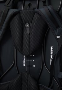 Svart ergonomisk ryggsekk med en struktur som har heksagonale polstrede seksjoner, justerbare høydeindikatorer og slitesterke stropper i et stilrent design.