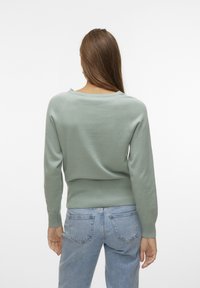 Pull vert menthe avec un col rond et des poignets côtelés, associé à un jean bleu clair avec poches au dos et une coupe décontractée.