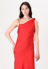 Raudonas su vienu petimi suknios su tekstūruota langeline raštu, turinti plonas petnešas ir juosmens lygyje esančią šoninės skilimą. Lengvas audinys su lygiu paviršiumi.