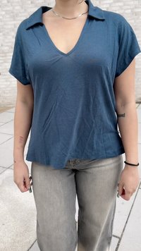Kortermet v-hals topp i mørk blått stoff med en avslappet passform; har krage og lett teksturert overflate. Kombinert med lys grå jeans.