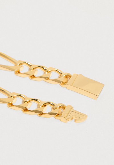 Primer plano de eslabones de cadena en tono dorado, con un extremo que presenta un cierre rectangular y el otro un conector estilizado en forma de llave.