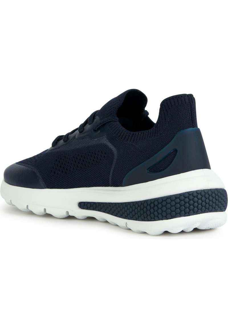 Zapatilla de deporte azul marino con parte superior de punto, soporte plástico en el talón, media suela blanca y suela exterior de goma texturizada. Presenta perforaciones sutiles para una mejor transpirabilidad.