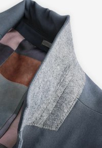 Dunkler Stoffkragen mit einem grauen Filzakzent. Gefüttert mit einem mehrfarbigen Patchwork-Design, das sanfte Töne von Blau, Braun und Grau aufweist.