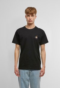 Black cotton t-shirt with short sleeves, featuring a small embroidered graphic on the chest. Straight cut and soft texture.