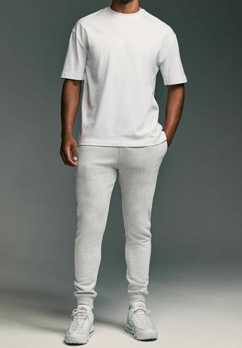 Hvid bomulds t-shirt med korte ærmer, parret med lysegrå sweatpants lavet af blødt stof. Suede sneakers med mesh detaljer.
