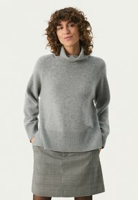 Grå turtleneck sweater med ribbet kant og manchetter, der har en blød striktekstur. Sammen med en grå ternet nederdel.