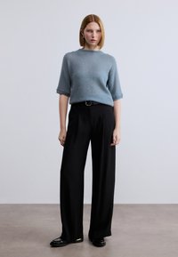 Ανοιχτό μπλε, κοντομάνικο πουλόβερ από απαλό ύφασμα, συνδυασμένο με μαύρο, ψηλόμεσο παντελόνι με φαρδιά μπάσκα και μαύρα μοκασίνια με χρυσή λεπτομέρεια.