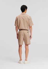 Camisa de cuello de manga corta y pantalones cortos a juego en una tela color tostado con patrones circulares, con un corte relajado y zapatillas blancas.