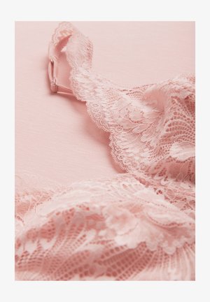Delicaat roze kanten beha met bloemenpatronen en verstelbare band, gelegd op een zachte roze stoffen achtergrond.