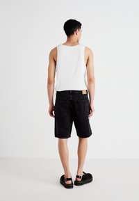 Pantaloni scurți din denim negru cu croi drept, asortați cu un top alb fără mâneci. Caracteristicile includ două buzunare pe spate și o etichetă din piele bej la talie.