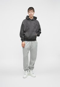 Ténis cinzentos com designs de estrelas, combinados com calças de moletão cinzentas claras e sapatilhas brancas. Tecido suave e corte descontraído. Sem padrões adicionais.