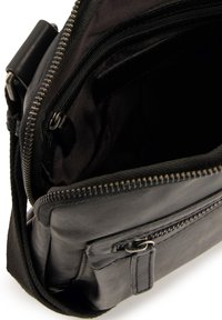 Černá kožená krosbody taška se zapínáním na zip, několik vnitřních kapes a texturovaným povrchem. Obsahuje odnímatelný popruh a zipový akcent.