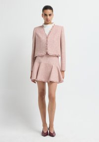 Lichtroze tweedpak met rafelige randen; getailleerde blazer met afgeronde zoom en een uitlopend mini-jurk. Draagt het met diep bordeauxrode hakken.